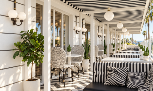 Art Deco café design at Hotel Shangri-La in Santa Monica, CA, by Karamia Designs combines bold black-and-white stripes, geometric flooring, and elegant globe lighting. Woven bistro chairs, tailored banquettes, and lush greenery create an inviting hospitality space that blends vintage glamour with relaxed coastal style.