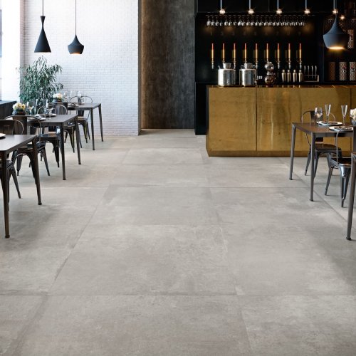 A modern and eye-catching restaurant located in downtown Los Angeles with an organic design style. The restaurant features industrial gray porcelain slabs on the walls, creating a modern and stylish atmosphere. The slabs have a textured surface, adding visual interest and depth to the space. The restaurant features an open floor plan with exposed beams and ductwork, maintaining an industrial charm. Large windows flood the space with natural light, creating a warm and inviting atmosphere. The furniture and decor incorporate elements of both modern and organic design, with clean lines and natural materials.
