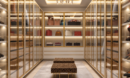 This luxury walk-in closet by Karamia Designs brings the elegance of a private boutique into the home. Gold-framed glass cabinetry and illuminated shelving beautifully display handbags, shoes, and wardrobe essentials while keeping everything organized. A sculptural crystal chandelier and warm cove lighting accentuate the recessed ceiling, while animal-print benches add a playful touch. Soft neutral finishes and a textured rug complete a sophisticated dressing room where custom closet design meets everyday comfort.